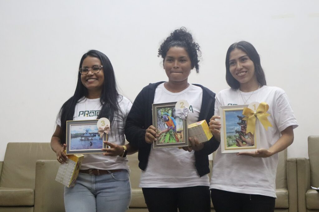 Três mulheres extrativistas sorriem enquanto olham para a camêra e seguram as fotos premiadas.